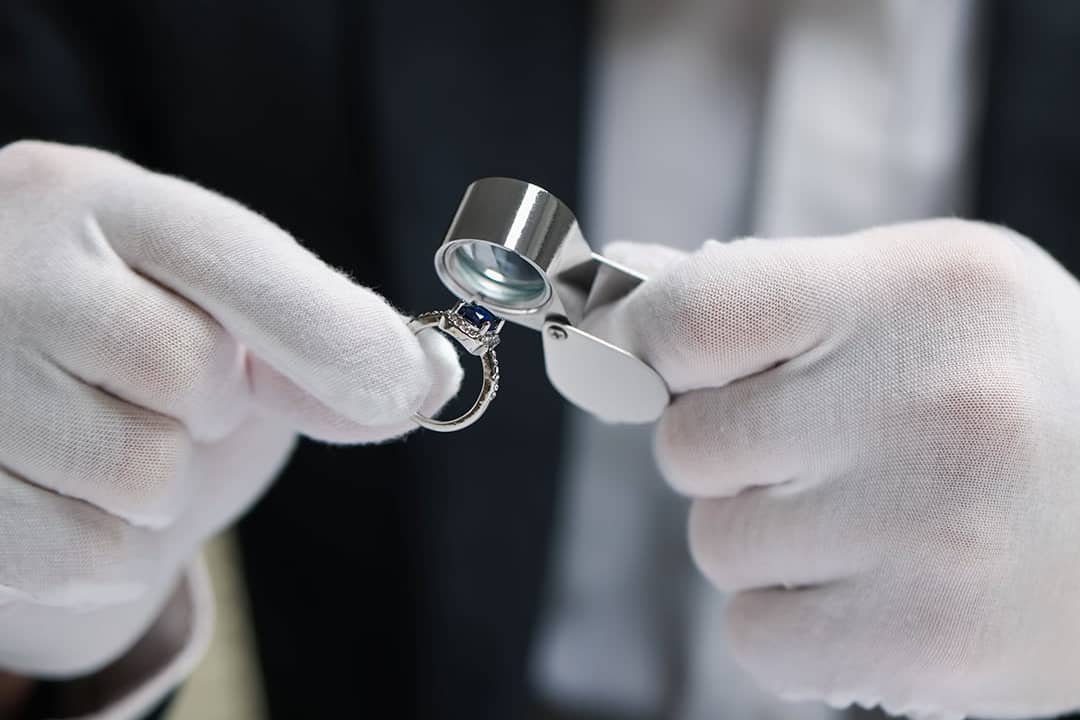 An appraiser evaluating a blue sapphire and diamond ring with a loupe.